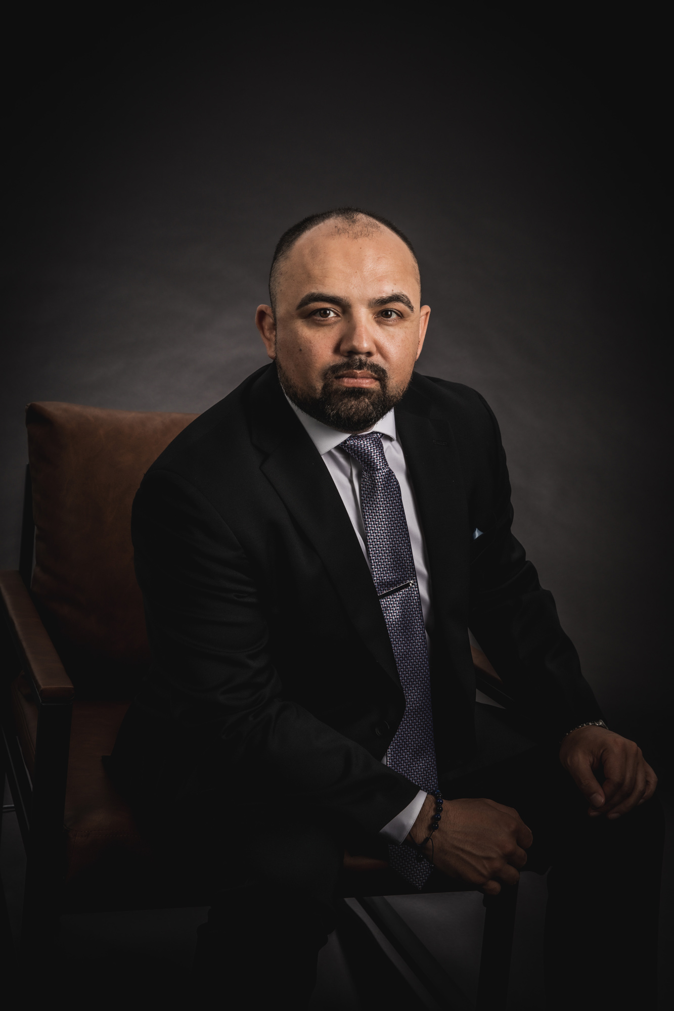 Low light and moody image of Angel Betancourt sitting in a leather chair with a dark background